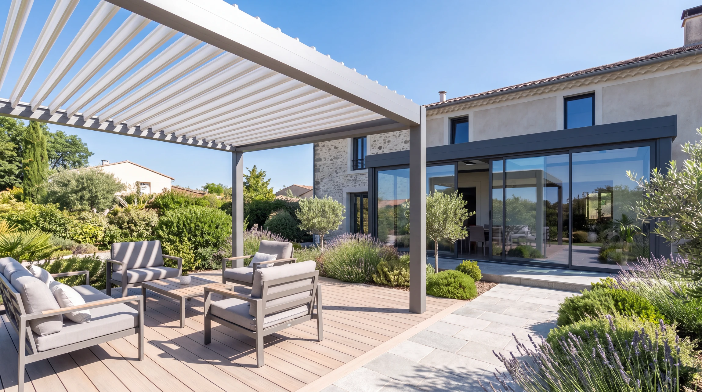 Terrasse extérieure moderne d'une maison individuelle avec une pergola bioclimatique en aluminium blanc ou anthracite aux lames orientables, intégrant aussi un carport attenant. La pergola couvre la terrasse en bois composite clair avec salon de jardin contemporain. À proximité, un carport moderne en aluminium ou acier gris anthracite abrite un véhicule. Véranda aluminium à baies vitrées coulissantes visible en arrière-plan, attachée à la maison. Végétation paysagée, dallage en béton ou grès cérame. Lumière naturelle mettant en valeur les structures métalliques et les menuiseries. Ambiance résidentielle haut de gamme, professionnelle et authentique.
