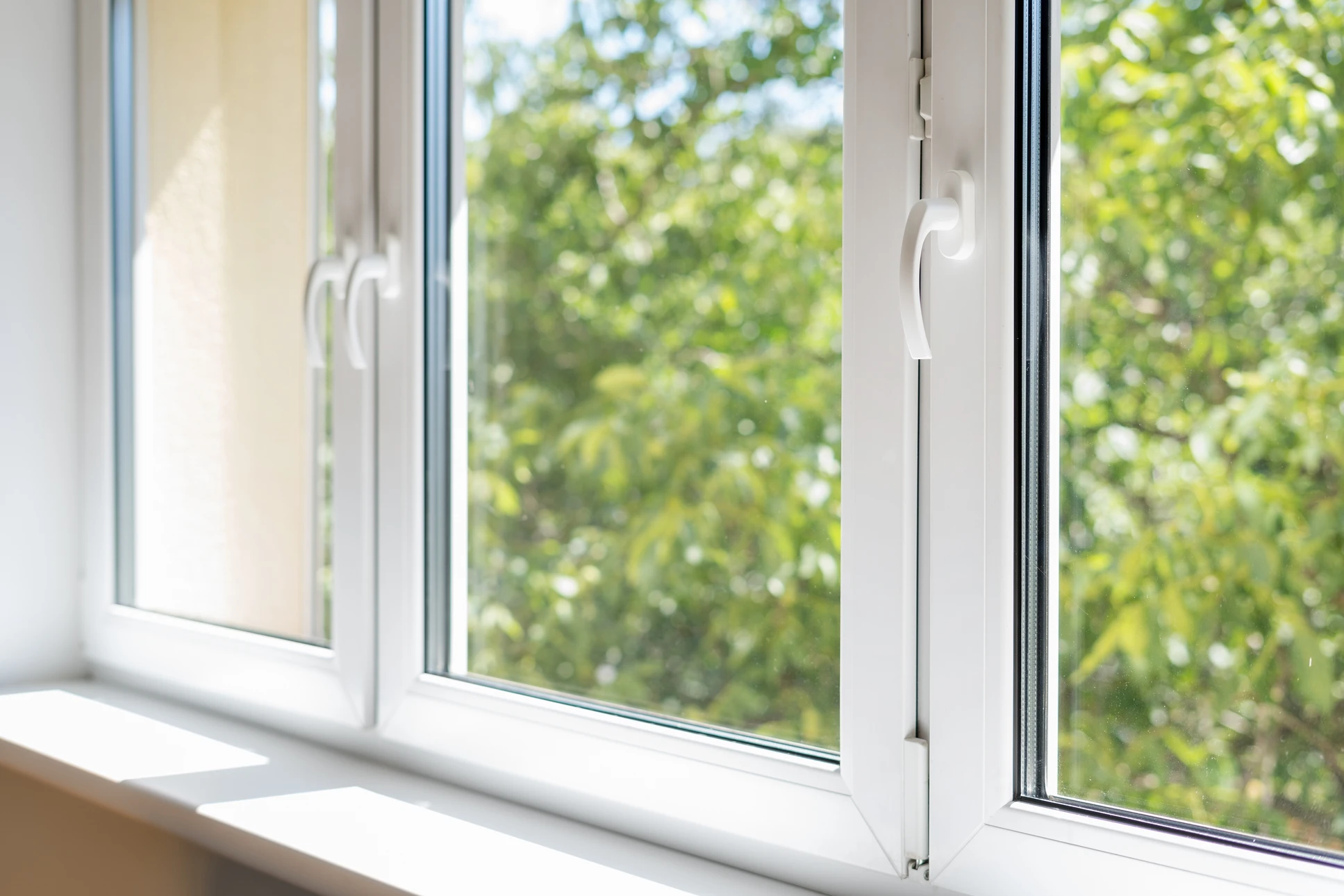 Main ouvrant une fenêtre moderne à double vitrage avec poignée beige dans un intérieur lumineux